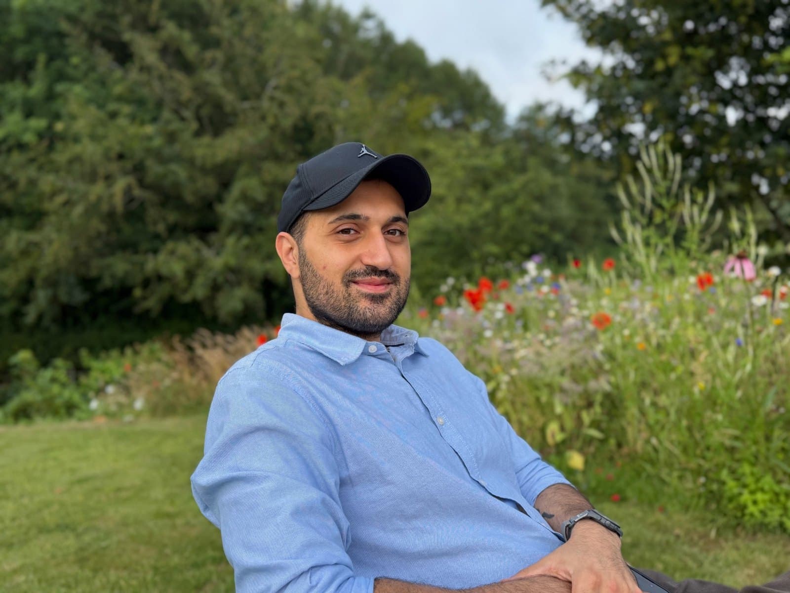 Mo in a blue shirt and cap, relaxing in a garden by a bed of poppies and wildflowers