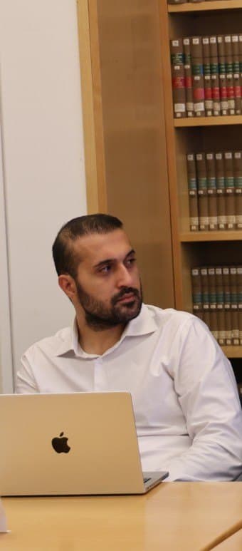 Mo at a research seminar, laptop open, in front of shelves of law reports